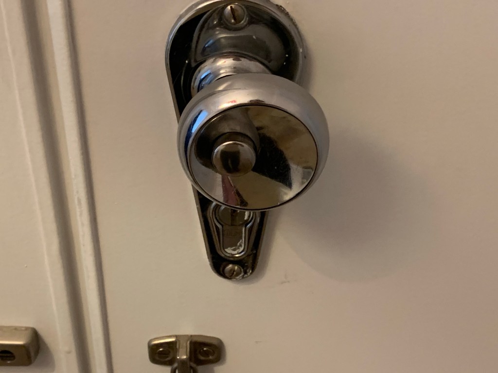 A concave silver doorknob with a button on it, slightly off-center to the left.
